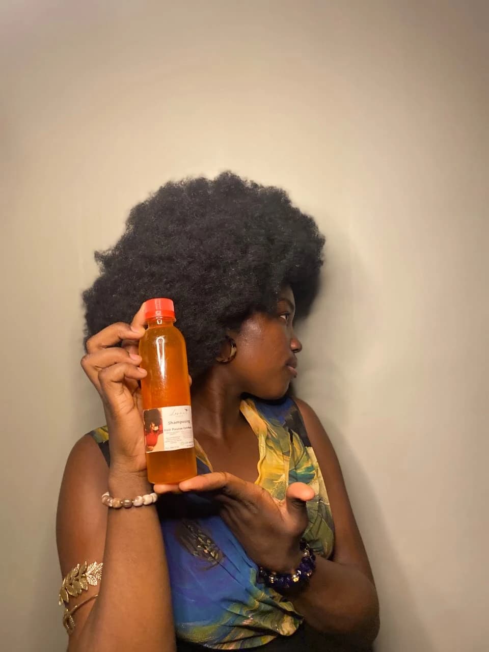 Femme aux cheveux afro volumineux, de profil, un flacon de soin à la main